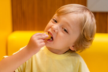 A small child wearing a yellow shirt is eating chicken nuggets in a vibrant environment. Four year old boy enjoying fast food meal. Kids diet, bad food choices, early junk food addiction