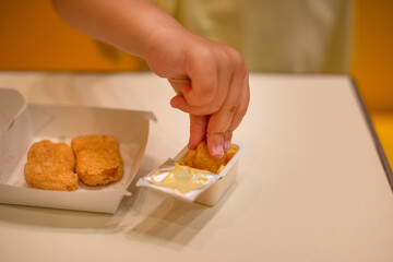 A small child wearing a yellow shirt is eating chicken nuggets in a vibrant environment. Four year old boy enjoying fast food meal. Kids diet, bad food choices, early junk food addiction