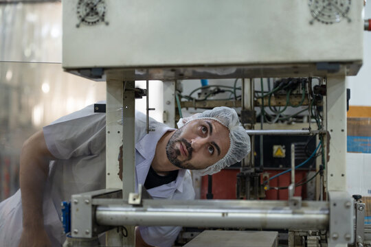 Male workers and inspectors in protective suits carefully manage and inspect the packing of processed food, canned fish on conveyor belt in food factory.