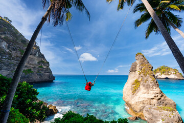 Young woman tourist on Bali swing at Diamond beach at Nusa Penida island Bali, Indonesia