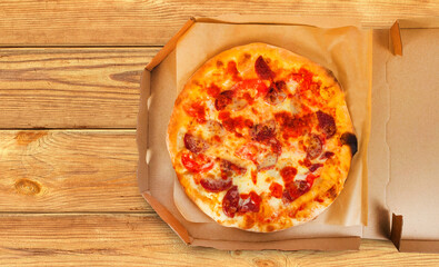 Photo of salami pizza in cardboard box on wooden table.
