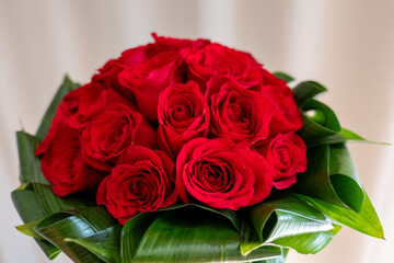 Bouquet of red roses (Rosa spp.) with decorative green leaves, arranged in a round floral design. Ideal for romantic occasions, weddings, or gifts.