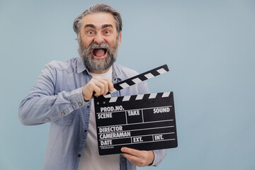 Excited senior film director using movie clapperboard on blue background