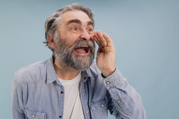 Enthusiastic senior man shouting and cupping hand around mouth on blue background