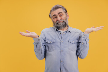 Puzzled senior man shrugging shoulders on yellow background