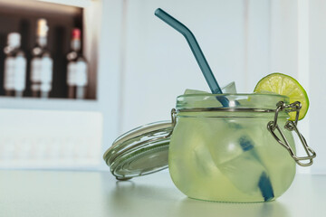 A chilled green cocktail served in a mason jar with a blue straw and lime slice garnish, placed on...
