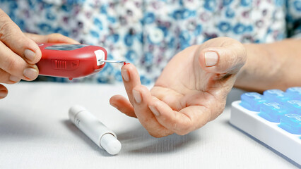 Blood glucose meter diabetes test senior hand pricking finger blood drop medical device home healthcare monitoring close up daily routine health management