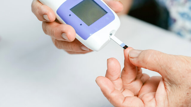 Blood glucose meter diabetes test hand finger medical device healthcare monitoring close up elderly measurement. This close up image shows person using blood glucose meter to check blood sugar