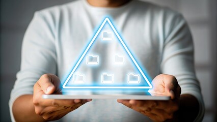 A person holds a tablet displaying a glowing triangular hologram with digital folder icons, symbolizing data organization and technology.