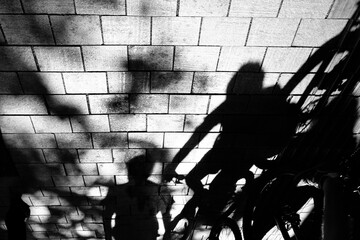 Shadow silhouette of cyclists riding bike on city sidewalk, in black and white high contrast