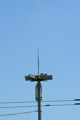 A tall pole with a light on top of it. The pole is surrounded by wires and the sky is clear