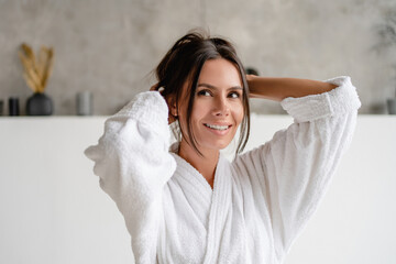 Naklejka premium Happy attractive brunette lady stretching hands enjoying morning beauty routine in luxury bathroom indoors. Wellness and spa. Female relaxing in hotel bathing room on weekend looking aside away