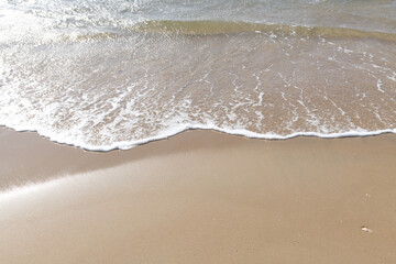 Sand beach with small sun lit waves.