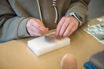 Close-up of hands using needle felting technique, meticulously shaping wool fibers on a foam block, creating intricate designs with precision and artistry