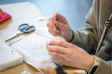 Close-up of craftswoman hands creating wool felt figure using needle felting technique, showcasing the process of transforming wool fibers into art