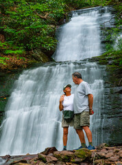 A senior couple share a tender moment together after hiking through the woods to a beautiful waterfall.