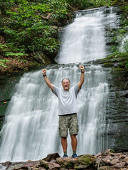 Active senior man in his 70's celebrates his climb up to a waterfall