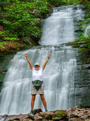 Active senior woman celebrates her climb up to a waterfall