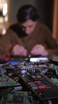 A deep and technical mood is captured by a close-up of computer circuit boards and components in the foreground, with a blurred technician actively working on them in the background