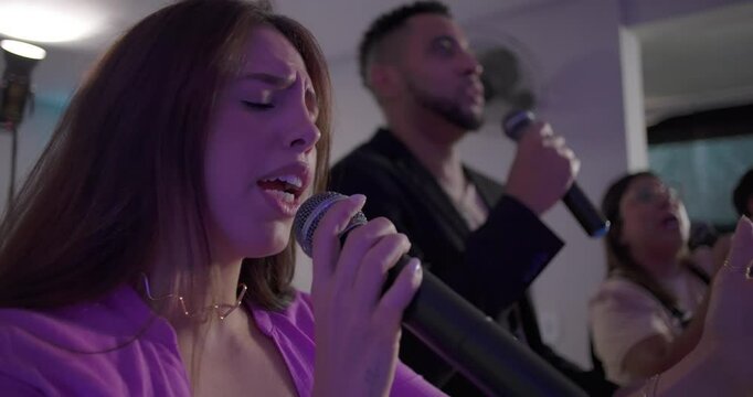 Young woman sings passionately into microphone with eyes closed during church worship, accompanied by backup vocalists in small spiritual gathering