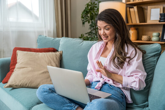 Happy woman at home using laptop for online dating video call. Excited young female meets love interest through webcam chat, enjoying virtual romantic connection and digital relationship experience.