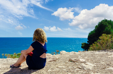 Curly-haired blonde woman looking at the sea in Torredembarra, Tarragona