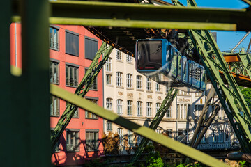 Eine Schwebebahn fährt zwischen alten Industriegebäuden in der Nähe der Haltestelle Kluse,...
