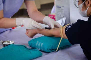 Close up nurse pricking needle syringe in the arm patient drawing blood sample for blood test , Health check