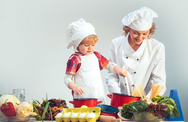 Mother and chef child cooking together. Chef Kid helping mom in kitchen. Mother and son cooking meal. Child in chef hat with Mother in chef apron on kitchen. Mom and son cooking at home.