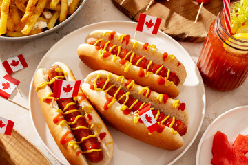 Top view of Canada Day party food with poutine, hot dogs, fruit, skewers, and donuts decorated with Canadian flags