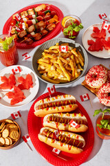 Top view of Canada Day party food with poutine, hot dogs, fruit, skewers, and donuts decorated with Canadian flags