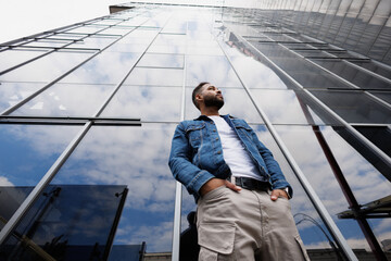 Low angle view of african american man in street wear standing near building with glass facade