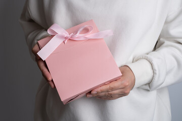 Pink box with pink ribbon in girl's hands. Space for text and logo. Gift wrapping