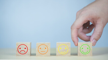 Wooden cubes with different emoji faces ranging from sad to happy, with a hand selecting the happy...
