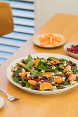 Fresh spinach salad with tangerines, pomegranate and cheese on wooden table