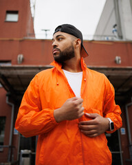 Portrait of african american man in vivid windbreaker jacket and baseball cap standing on street