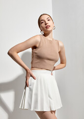 A stylish slender woman in a summer tank top poses against a light background showing off her clothes