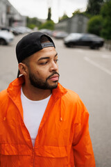 Portrait of african american man in baseball cap and orange windbreaker standing on street