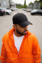 Young african american man in baseball cap and windbreaker standing on street