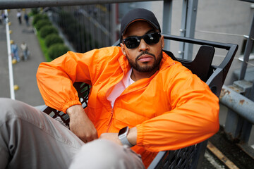 Trendy african american man in sunglasses sitting in shopping cart outdoors 