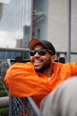 Positive african american man in sunglasses having fun in shopping cart on street
