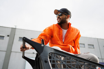 Smiling african american man in sunglasses sitting in shopping cart on street