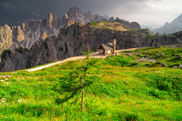 Tourists walking on a picturesque mountain trail. Cadini di Misurina, Dolomites, Veneto, Italy, Europe. Church against the background of mountains.	
