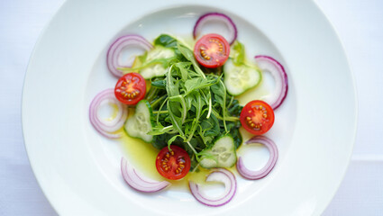 Fresh Green Salad with Red Cherry Tomatoes Sliced Cucumbers and Red Onion Rings on a White Plate Overhead View