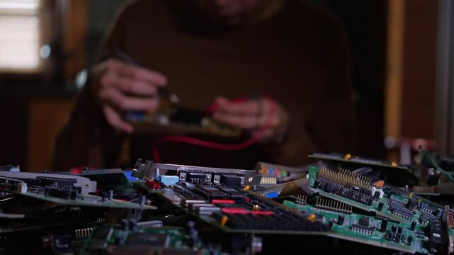 A complex and industrious mood is captured by a close-up of numerous computer circuit boards in the foreground, with a blurred technician actively working on electronics in the background