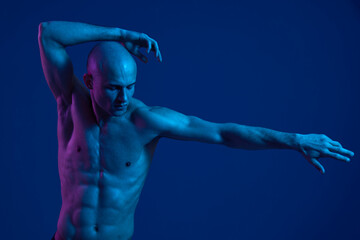 Dynamic male dancer posing with graceful movements, highlighted by vivid blue and pink lighting, showcasing strength and artistry in a visually striking performance.