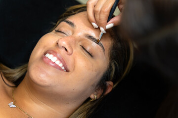 Naklejka premium Beautician applying eyebrow lamination to smiling latin woman