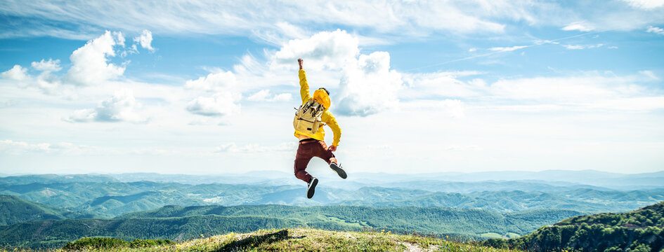 Happy man with backpack jumping on top of the mountain - Delightful hiker with arms up standing over the cliff - Sport and travel life style concept - Powered by Adobe