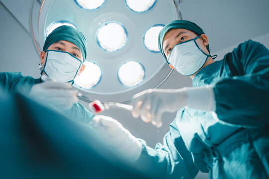 Low angle view, two Professional team confidence surgeon doctor performing surgery operation in theater operating room with medical instrument, tool, equipment. Healthcare, Hospital emergency concept