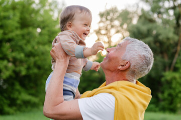 A happy grandfather holds a laughing baby up in the air, both looking at each other with pure joy...